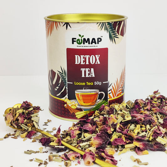 A tin can labeled 'FEMAP Detox Tea' alongside loose tea leaves and dried flowers scattered around.