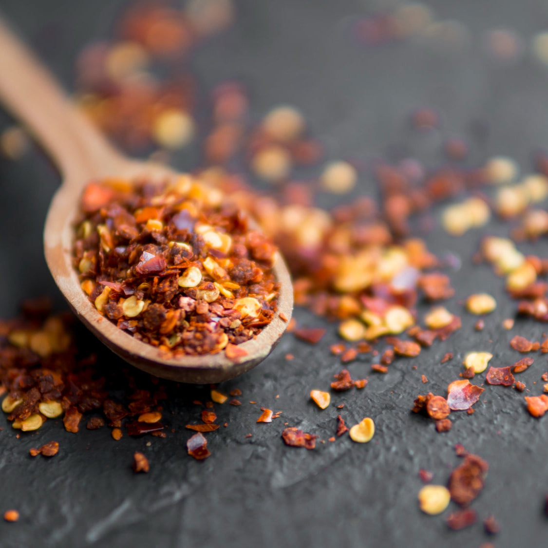 FEMAP premium red chilli flakes in wooden spoon on black background