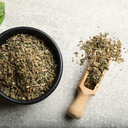 Dried herbs in a black bowl and wooden scoop on a textured surface