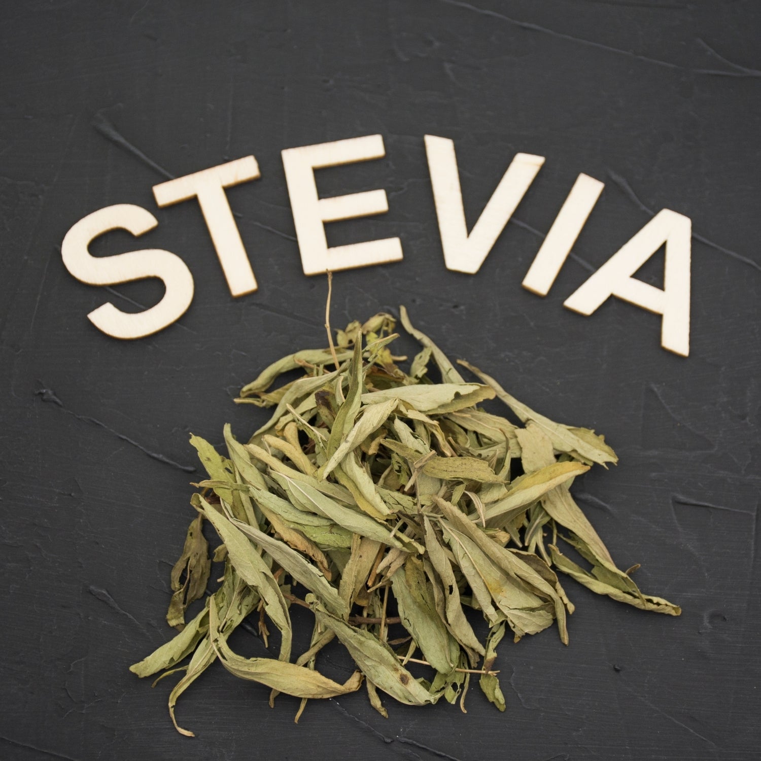 Dried stevia leaves with the word 'STEVIA' spelled out on a dark background