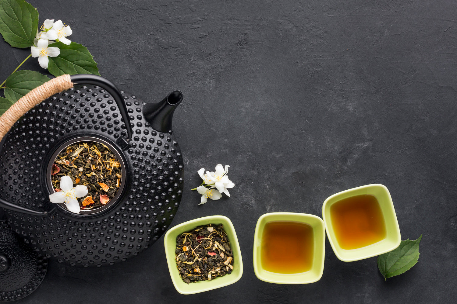 A Black ceremic tea pot and cup with full of herbal tea ingredients and tea in cup